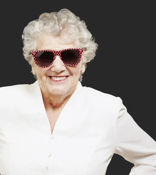Portrait of senior woman standing wearing sunglasses over black — Stock Photo, Image