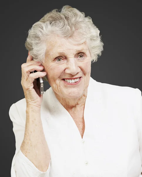 Porträt einer Seniorin, die auf ihrem Handy vor schwarzem Hintergrund spricht — Stockfoto