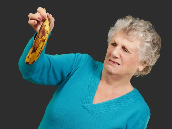 Ανώτερος γυναίκα που κρατά μια σάπια μπανάνα πάνω από το μαύρο φόντο — Φωτογραφία Αρχείου