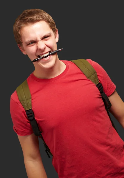 Портрет разгневанного молодого человека, кусающего ручку на черном фоне — стоковое фото