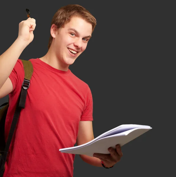 Портрет красивого студента, держащего тетрадь и ручку на черном — стоковое фото