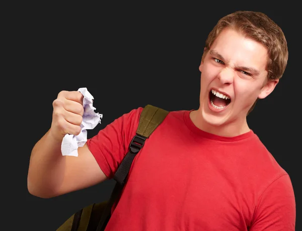 Fiatal dühös diák ember nagyoló egy lapot, mint fekete háttér — Stock Fotó