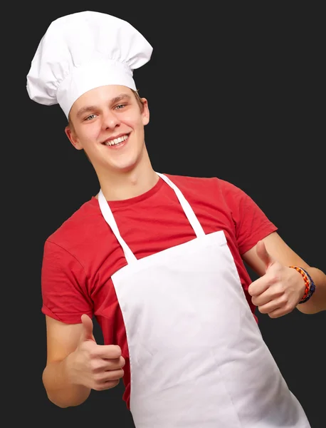 Retrato de jovem cozinheiro fazendo símbolo de sucesso contra um preto — Fotografia de Stock