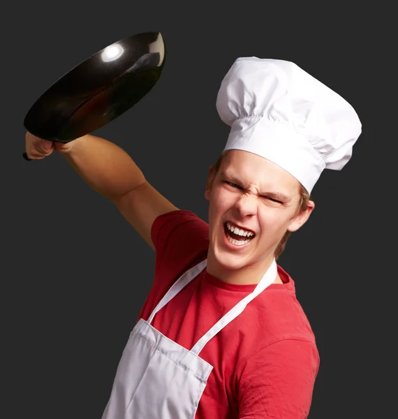 Портрет розлюченого молодого кухаря, який б'ється з каструлею над чорним спиною — стокове фото