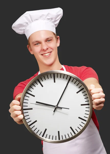 Portrait de jeune cuisinier homme tenant horloge sur fond noir — Photo