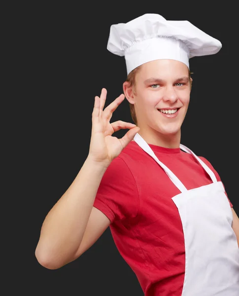 Retrato del joven cocinero haciendo símbolo de éxito sobre respaldo negro — Foto de Stock