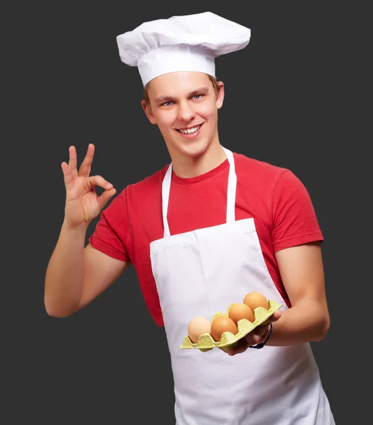 Ritratto di giovane cuoco che tiene la scatola delle uova e fa buon gesto — Foto Stock