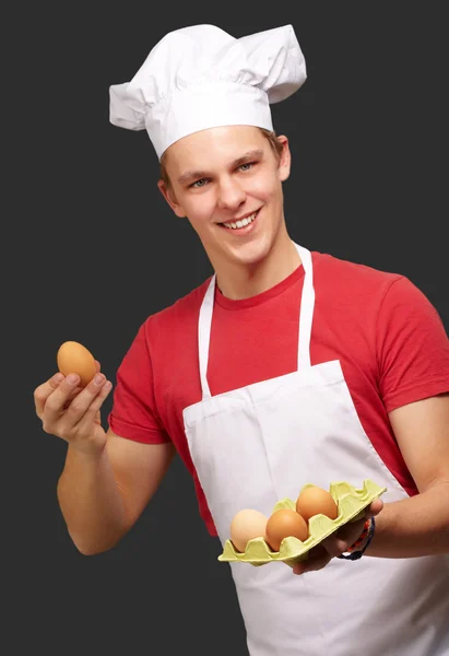Retrato del joven cocinero sosteniendo la caja de huevo sobre fondo negro — Foto de Stock