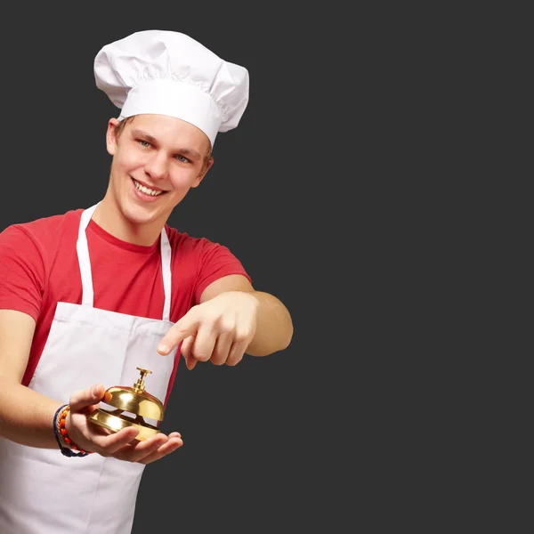 Retrato del joven cocinero presionando una campana dorada sobre bac negro — Foto de Stock