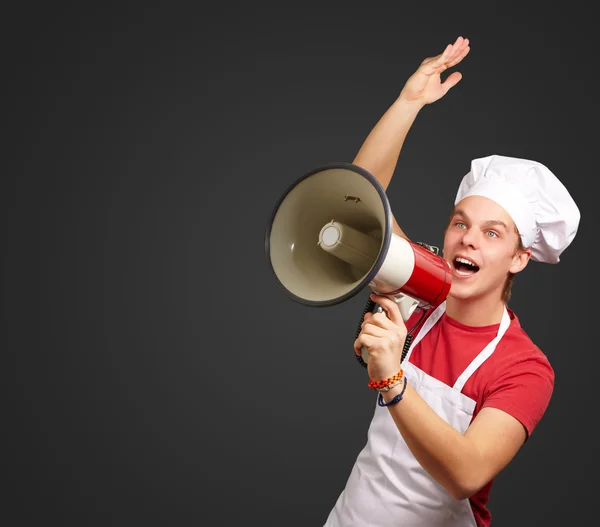 Portrait de jeune cuisinier homme criant avec mégaphone sur ba noir — Photo
