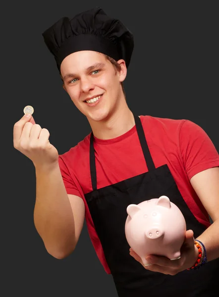 Retrato del joven cocinero sosteniendo moneda de euro y alcancía —  Fotos de Stock