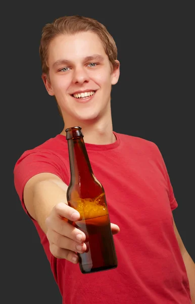 Portrait of young man holding beer against a black background — Stock Photo, Image
