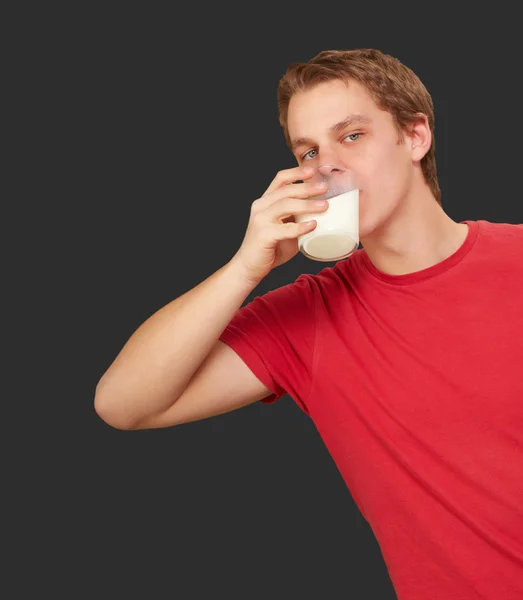 Portrait of young man drinking milk over black background — Stock Photo, Image