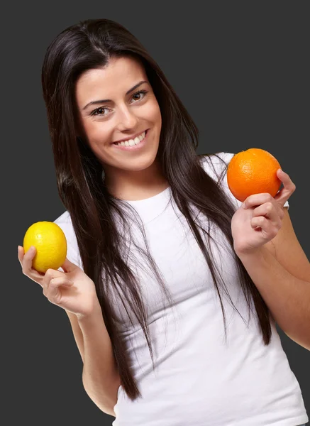 Молодая красивая девушка держит оранжевый и лимон на черном фоне — стоковое фото