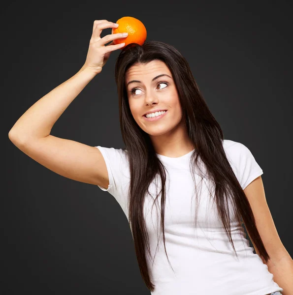 Retrato de mujer joven sosteniendo naranja en su cabeza sobre negro —  Fotos de Stock