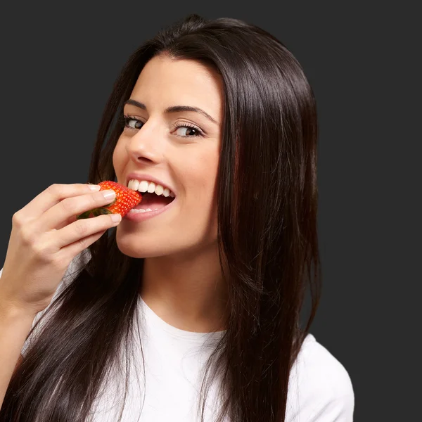 Porträtt av ung kvinna äta jordgubbar mot en svart bakgrunds — Stockfoto