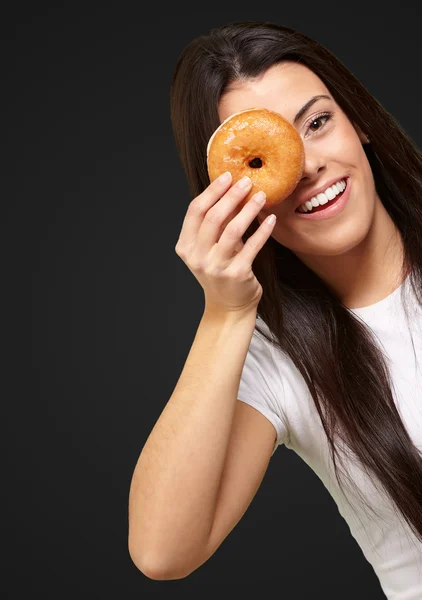 Retrato de jovem mulher olhando através de um donut sobre preto — Fotografia de Stock