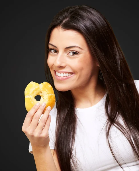 Retrato de jovem mulher comendo um donut sobre preto — Fotografia de Stock