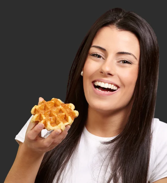 Portrait of young woman holding waffle over black background — Stock Photo, Image