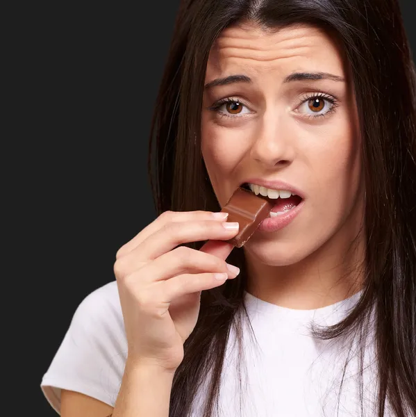 在黑色 backgrou 吃巧克力棒的年轻女人肖像 — 图库照片