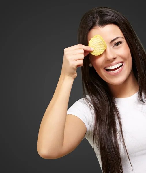 Portrait of young woman holding a potato chip in front of her ey — Stock Photo, Image