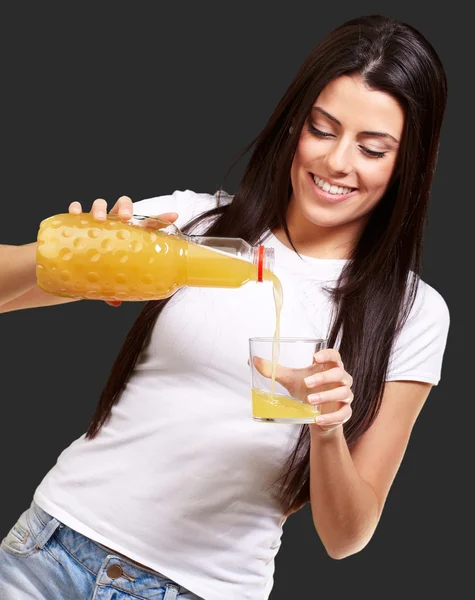 Portrait of young woman pouring orange juice on glass over black — Stock Photo, Image