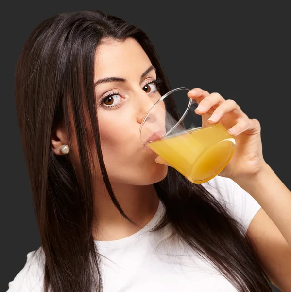 Portrait of young girl drinking orange juice against a black bac — Stock Photo, Image