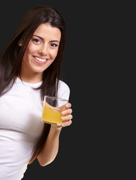 Portrait of young girl drinking orange juice against a black bac — Stock Photo, Image