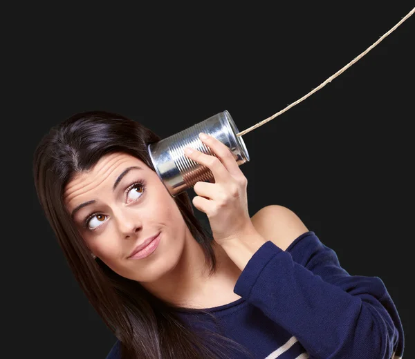 Portrait of young woman hearing through a tin can over black — Stock Photo, Image