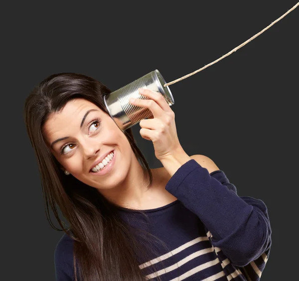 Young woman hearing using a metal tin can over black background — Stock Photo, Image