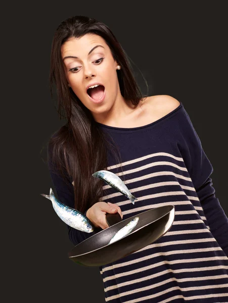Muotokuva nuori tyttö ruoanlaitto kuriton kaloja pannulla yli musta b — kuvapankkivalokuva