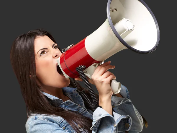 Portrait of young woman screaming with megaphone against a black — Stock Photo, Image