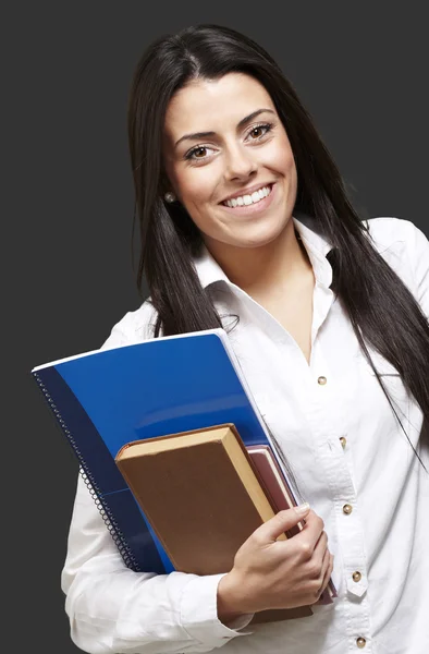 Junge Studentin hält Bücher in der Hand und lächelt vor schwarzem Hintergrund — Stockfoto