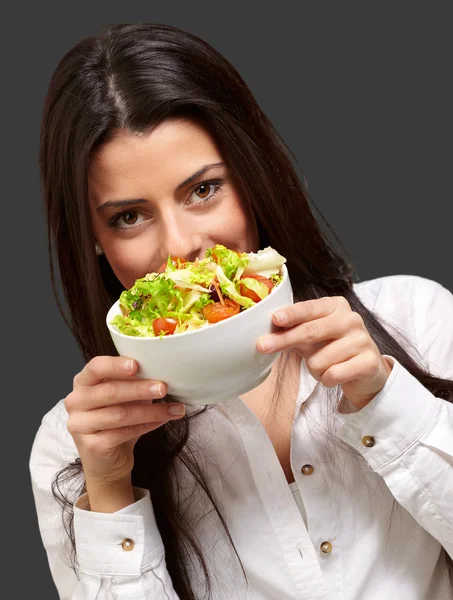 Portrait of young woman holding a fresh salad over black — Stock Photo, Image
