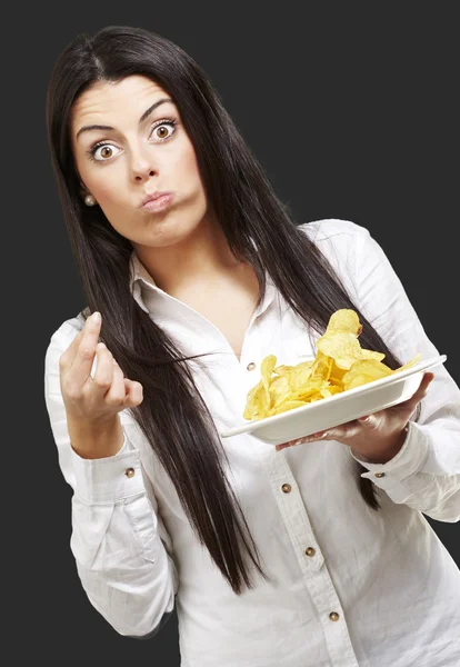 Mladá žena jíst brambůrky na černém pozadí — Stock fotografie