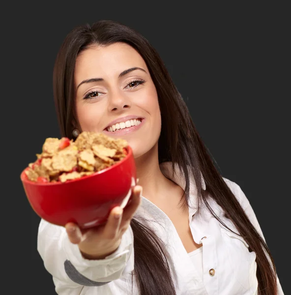 Portrait of young woman offering cereals bowl over black backgro — Stockfoto