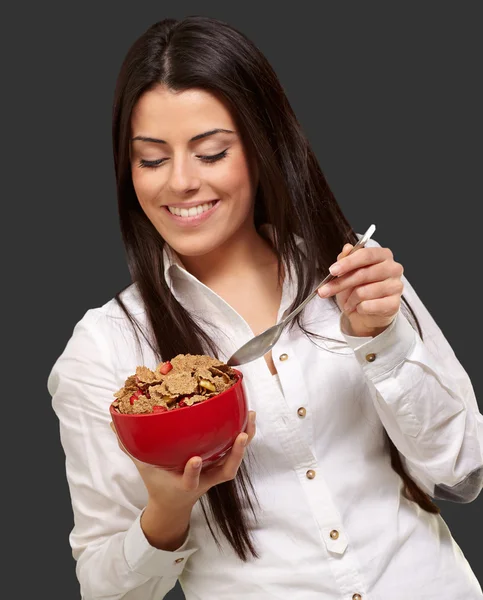 Portrait of healthy young woman eating cereals over black