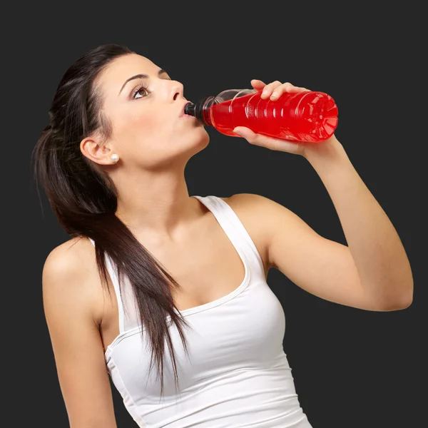 Portrait of young sporty woman drinking isotonic drink over blac — Stock Photo, Image