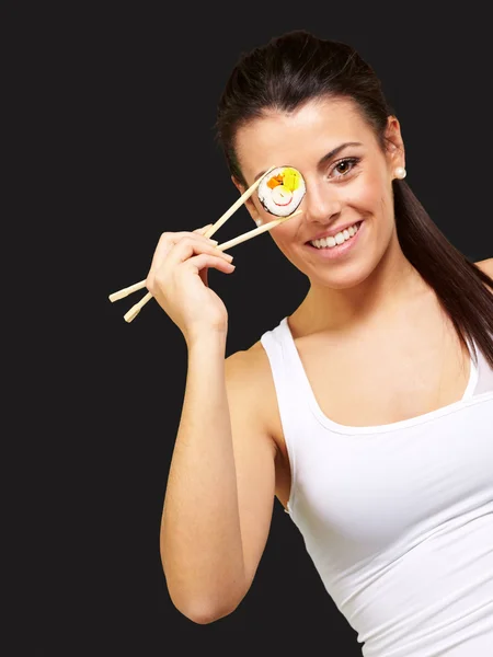Mujer joven cubriéndose el ojo con una pieza de sushi contra un negro —  Fotos de Stock