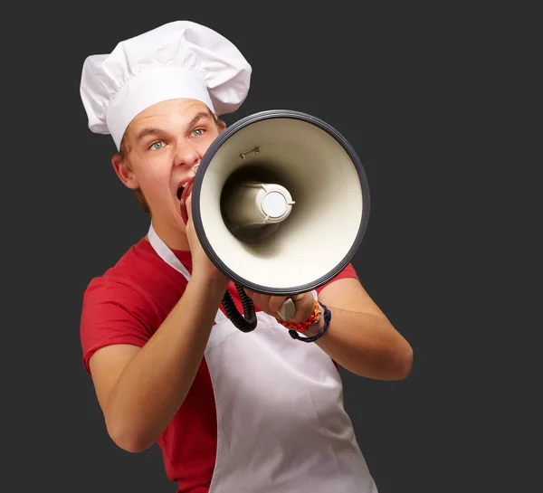 Portrait of young cook man screaming with megaphone over black b Royalty Free Stock Photos