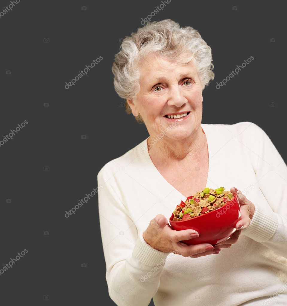 Portrait of healthy senior woman holding cereals bowl over black