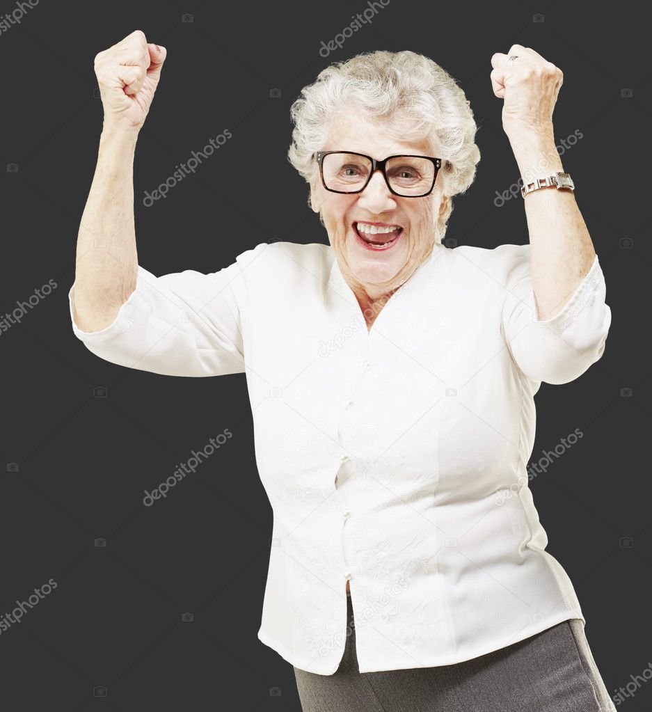 Portrait of a cheerful senior woman gesturing victory over black