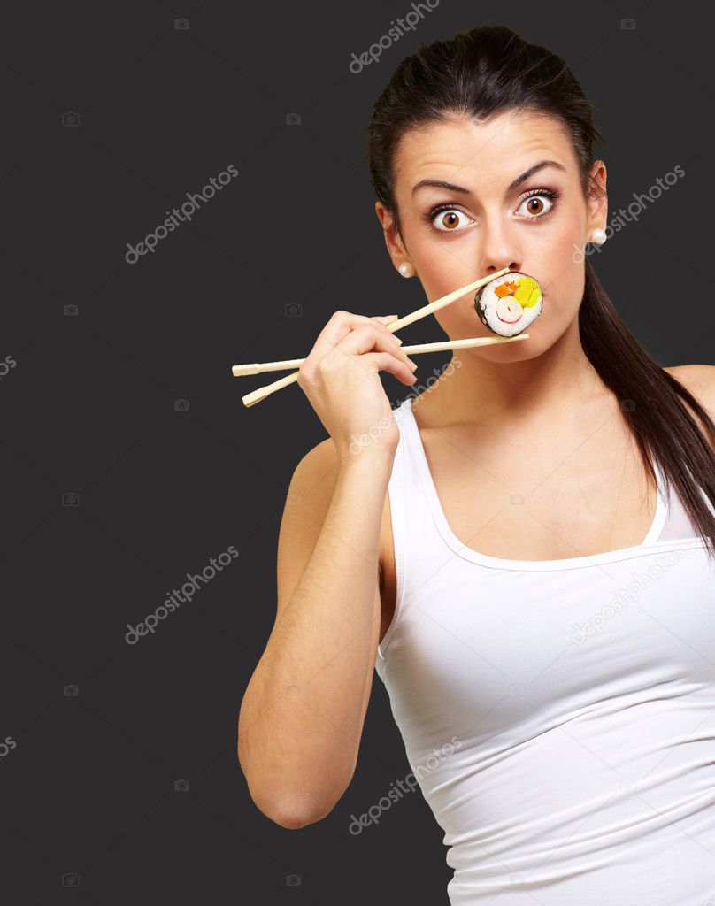 Young woman covering her mouth with a sushi piece against a blac