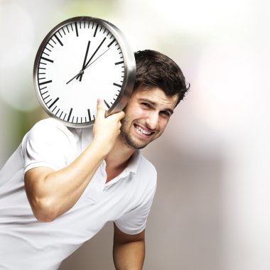 Portrait of a handsome young man carrying a clock against a blurry background clipart