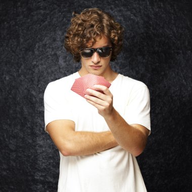 Portrait of young man wearing sunglasses and playing poker against a vintage background clipart