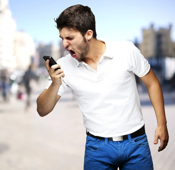 Porträt eines wütenden jungen Mannes, der mit seinem Handy auf einer belebten Straße schreit — Stockfoto