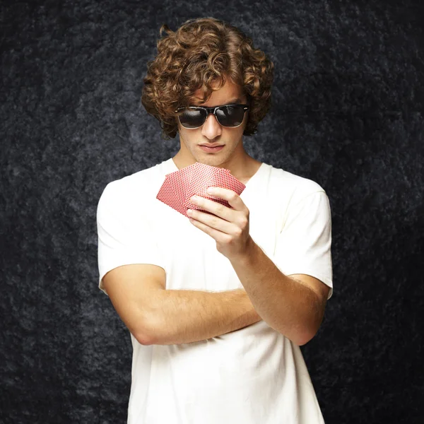 Portrait of young man wearing sunglasses and playing poker against a vintage background — Stock Photo, Image