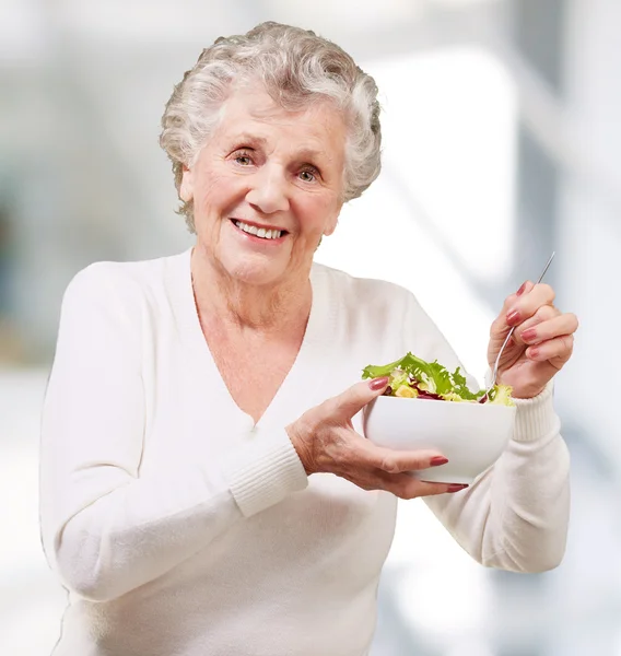 Portrét starší ženy jíst salát vnitřní — Stock fotografie