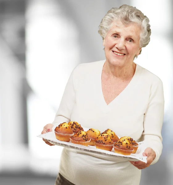 Porträtt av äldre kvinna visar hemlagade muffins inomhus — Stockfoto