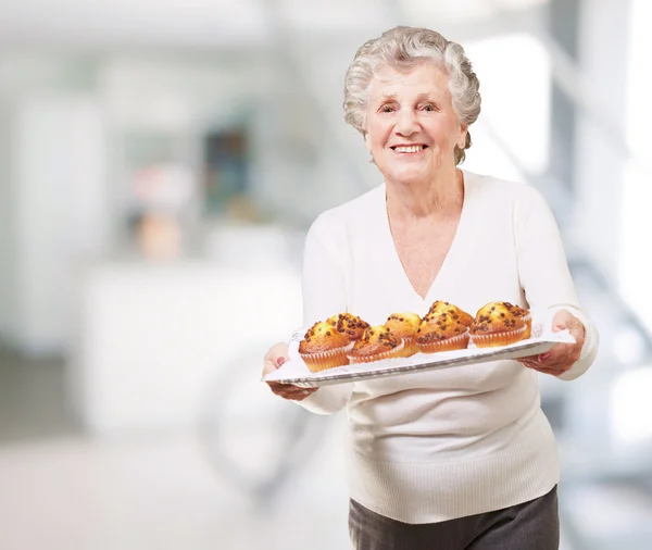 Portrait de femme âgée montrant un plateau de muffins au chocolat à l'intérieur — Photo